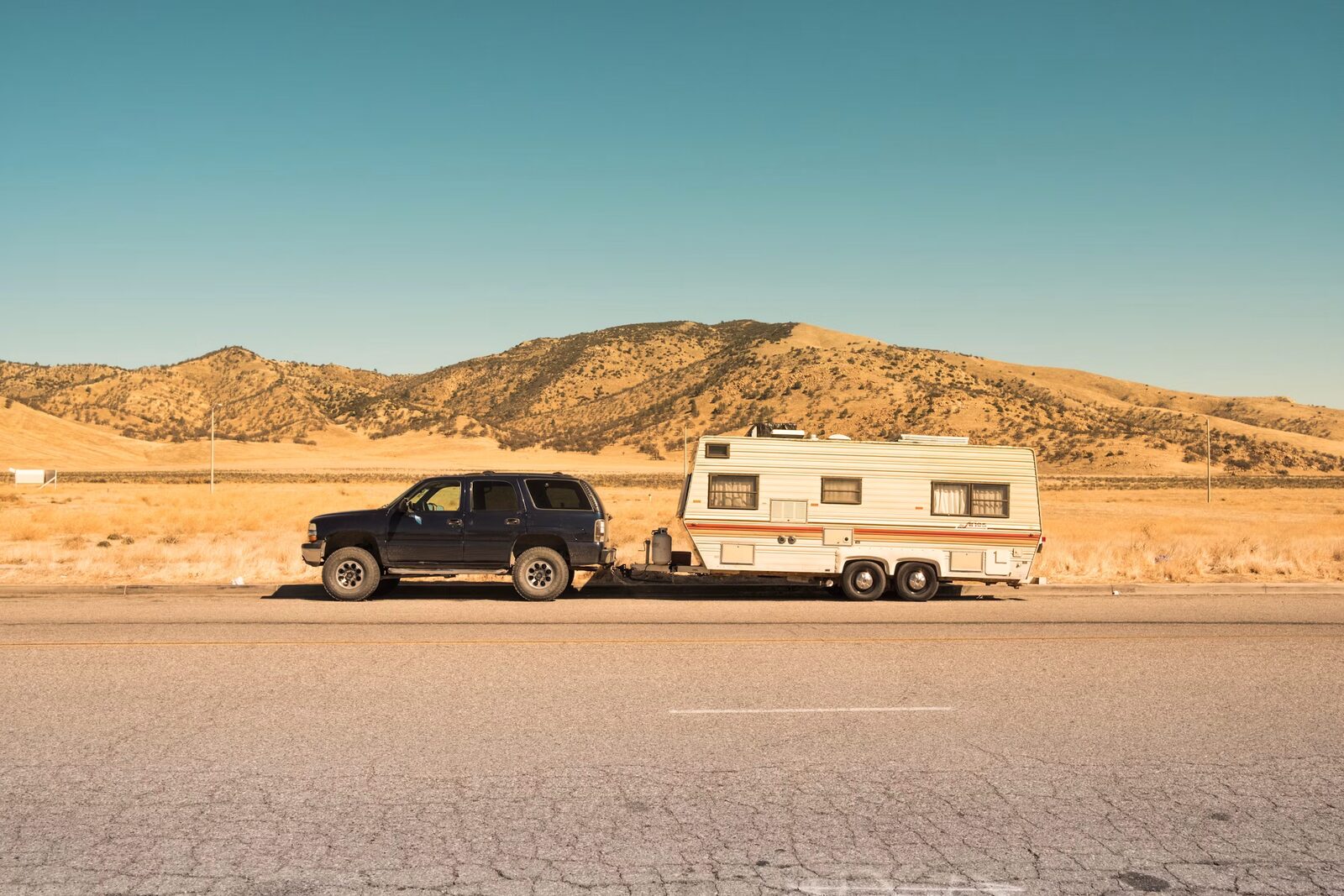 SUV hitched to vintage travel trailer against desert hills
